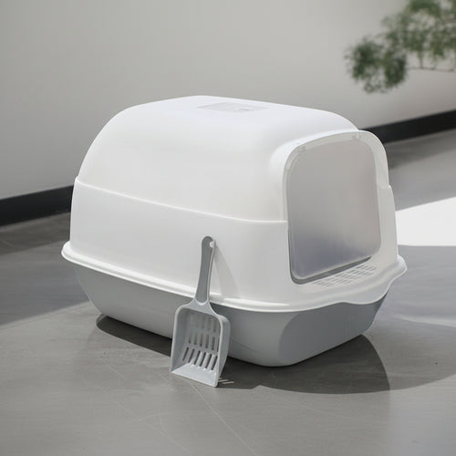 White cat litter box with a scoop on a gray surface.