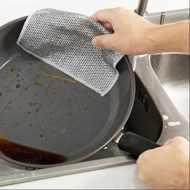 Person cleaning a greasy pan with a mesh scrubber in a kitchen sink.